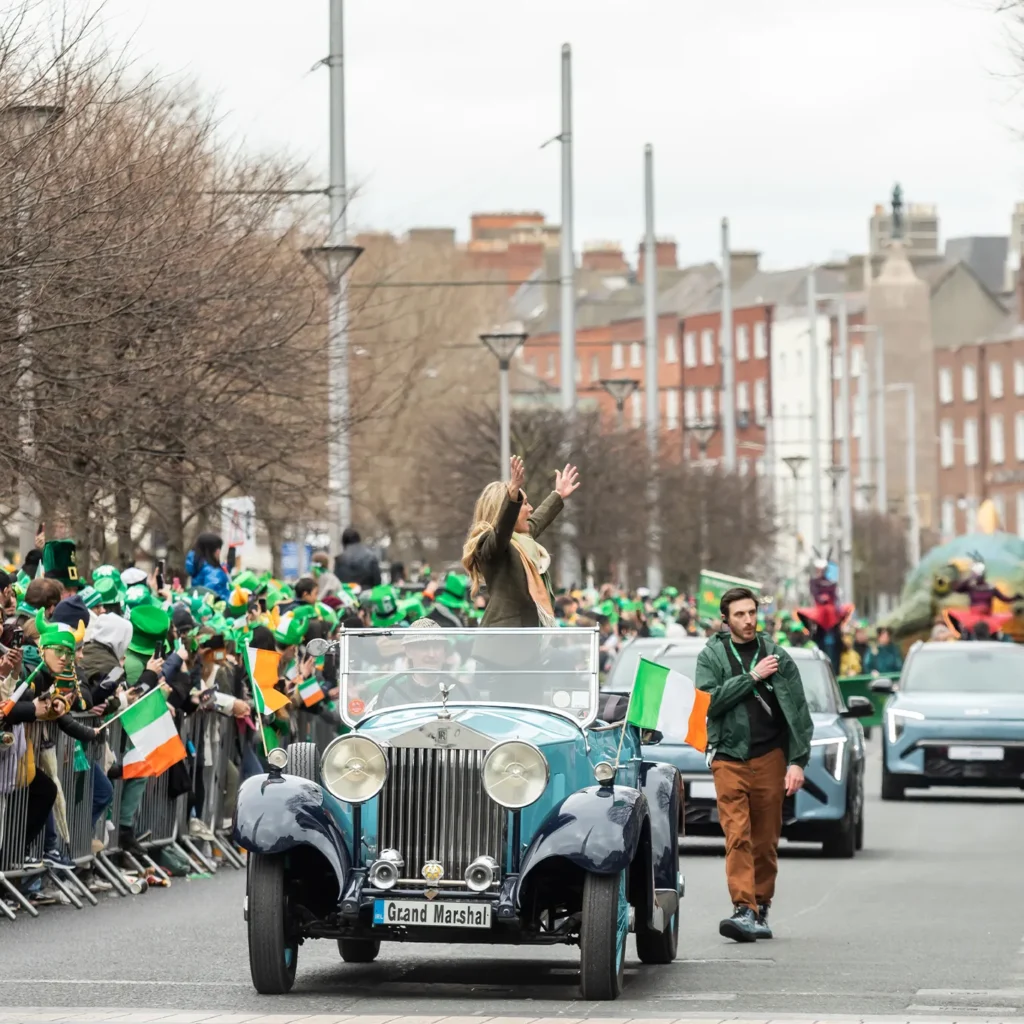 Grand Marshall stands up in car as it drives along parade